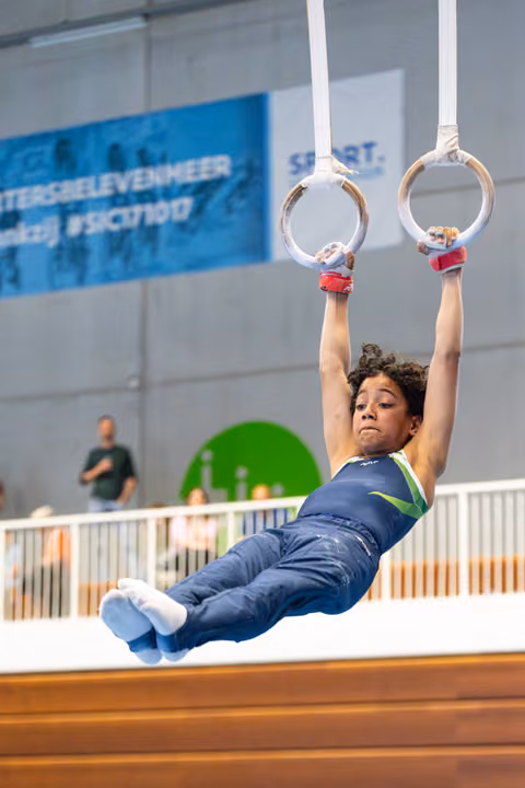 Young athlete performing on rings with intense concentration, body extended horizontally during indoor training session