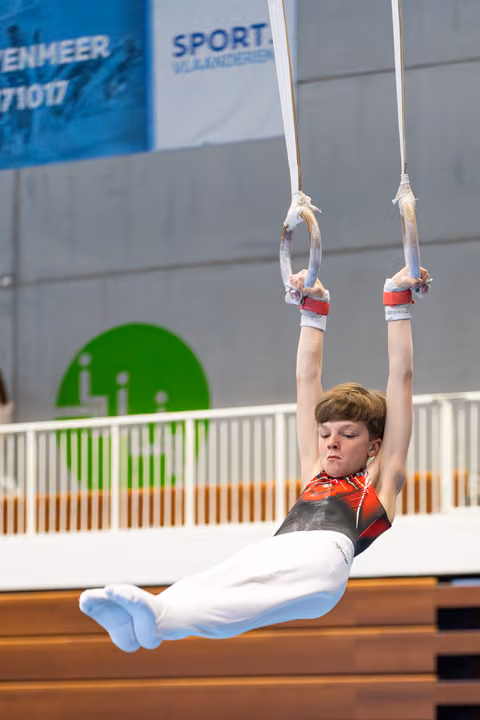 Young gymnast executing a hold position on still rings with straight body and pointed toes during indoor competition