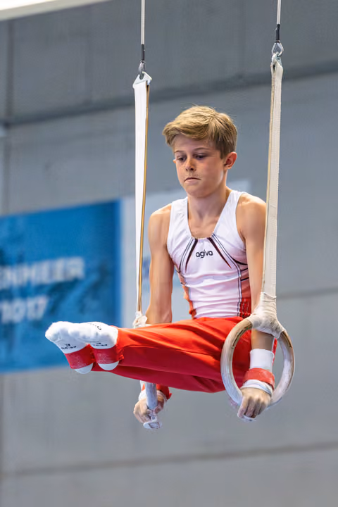 Young athlete performs on rings with intense concentration, body horizontal, wearing white and red uniform