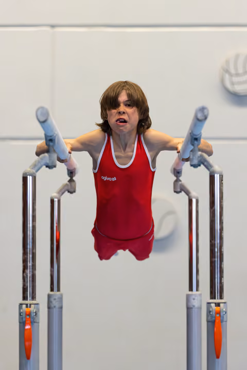 Young gymnast mid-routine on parallel bars, arms extended, showing intense focus and determination during competition