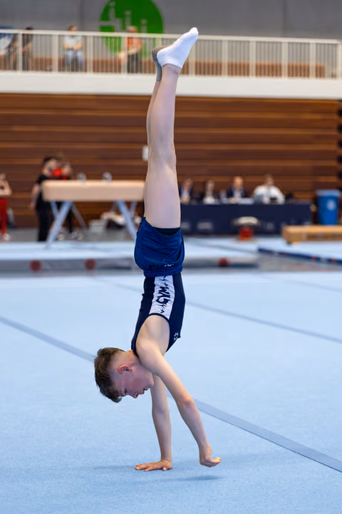 Young athlete performs a handstand during floor exercise routine at indoor gymnastics meet, demonstrating strength and balance