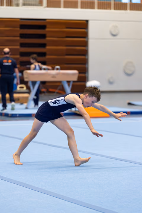 Young athlete performs a deep lunge position during floor exercise routine on blue training mat in gymnasium