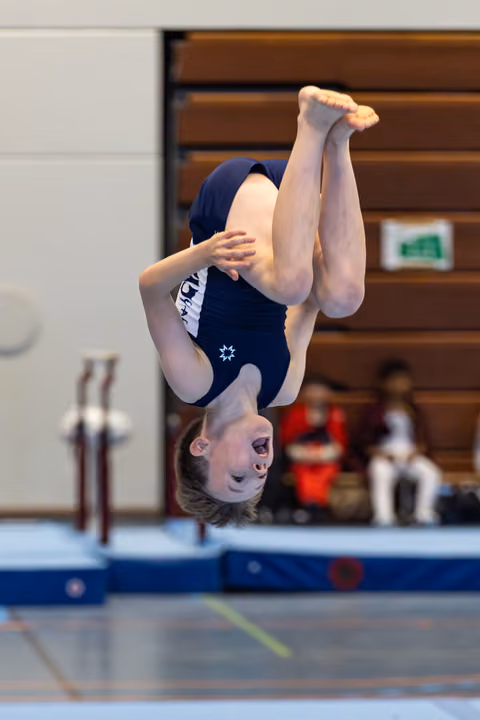 Young athlete performs a tucked backflip mid-air during a gymnastics competition in an indoor sports hall