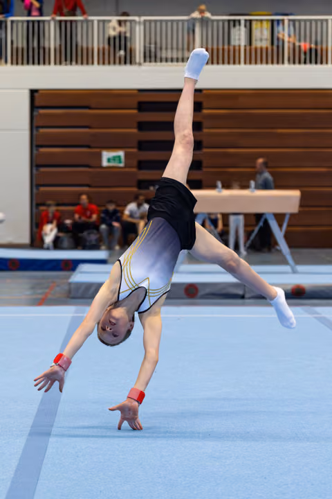 Young gymnast performs a cartwheel on floor exercise mat, wearing white and black leotard with red wrist guards