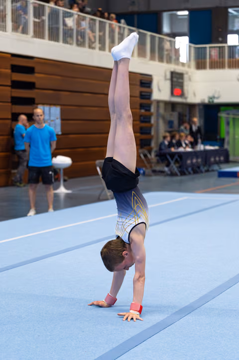 Young athlete executes a precise handstand with straight legs on the blue floor mat during a competitive routine