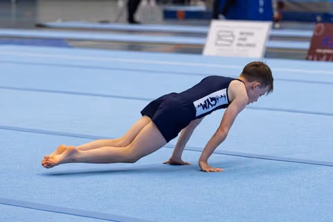 Young gymnast holds a perfect plank position on blue floor mat, demonstrating core strength and body control during training