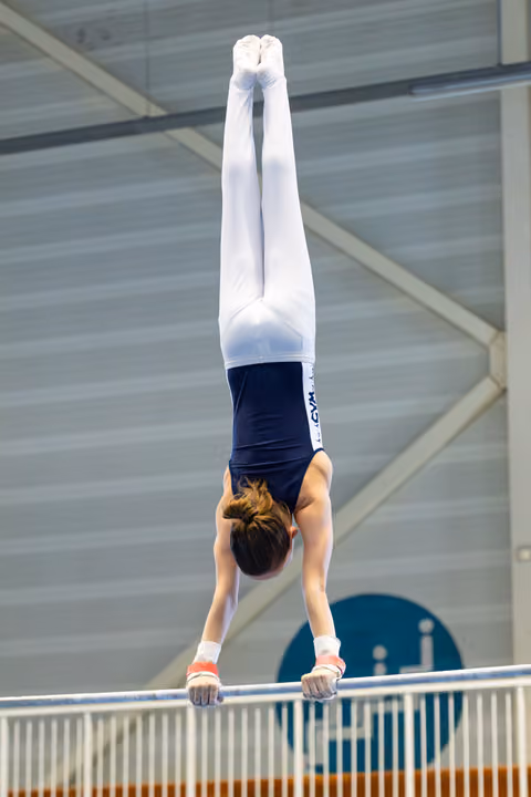 Young athlete performs perfect vertical handstand on parallel bars during indoor training session
