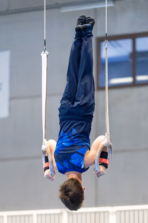 Young athlete performing an inverted hang on still rings, displaying strength and control during training