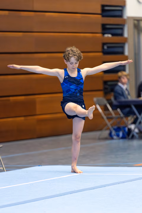 Young athlete performs a balanced T-pose during floor exercise routine, arms extended, one leg raised with pointed toe
