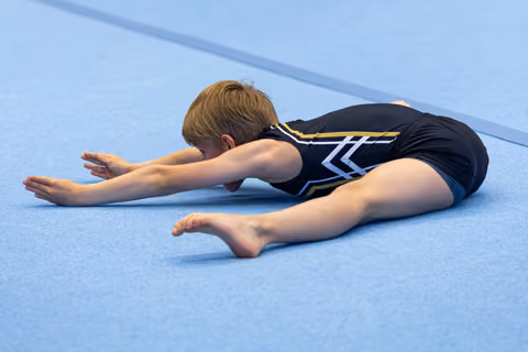 Young gymnast performing a forward fold stretch in splits position on blue floor mat during training
