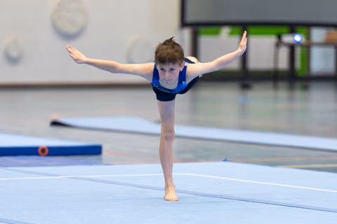 Young athlete performs arabesque balance with arms extended on floor mat, demonstrating poise and concentration