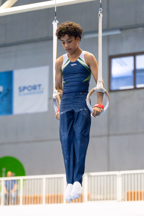 Athlete in navy uniform concentrates while suspended on rings, displaying focus and control in indoor training facility
