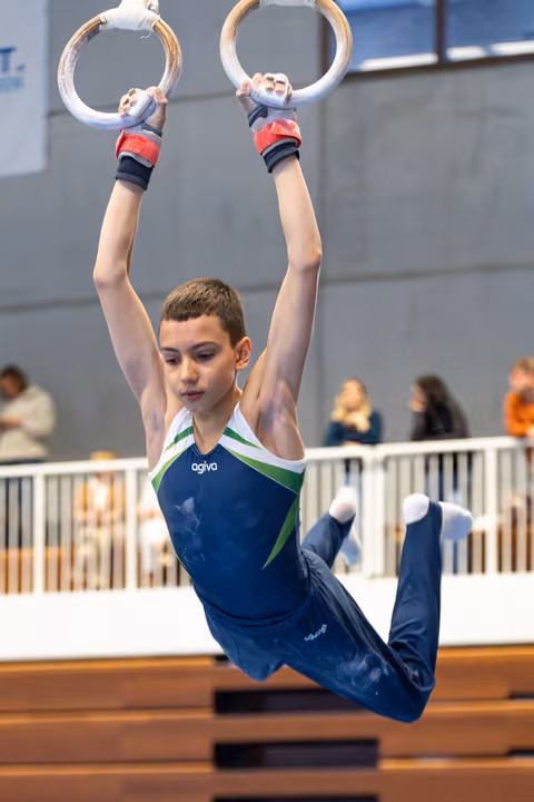 Young athlete hanging from rings with arms extended overhead, demonstrating strength and focus during indoor training session