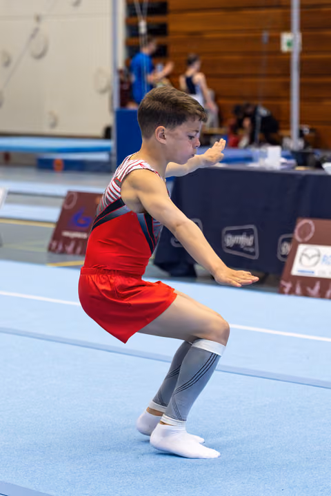 Young athlete in red outfit and knee-high socks maintains a focused squat position during floor exercise routine
