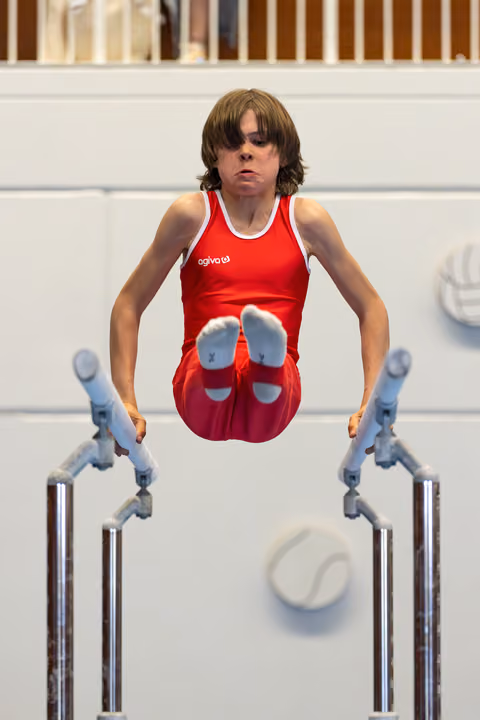 Young athlete performing on parallel bars with focused expression, demonstrating strength and control during routine