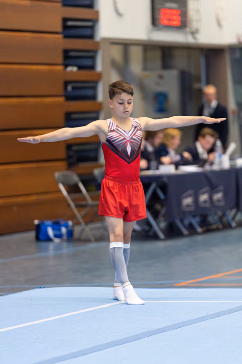 Young athlete performing a balance pose with outstretched arms during a floor routine at an indoor competition