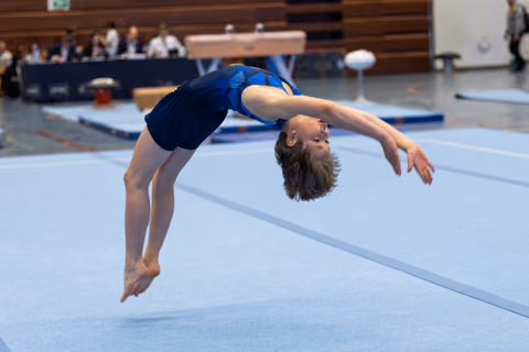 Young athlete executes a graceful backward arch mid-air during floor routine, arms extended with focused expression
