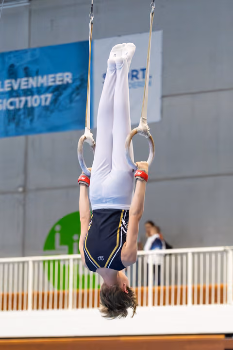 Young athlete performs inverted hang on rings during routine at indoor sports venue