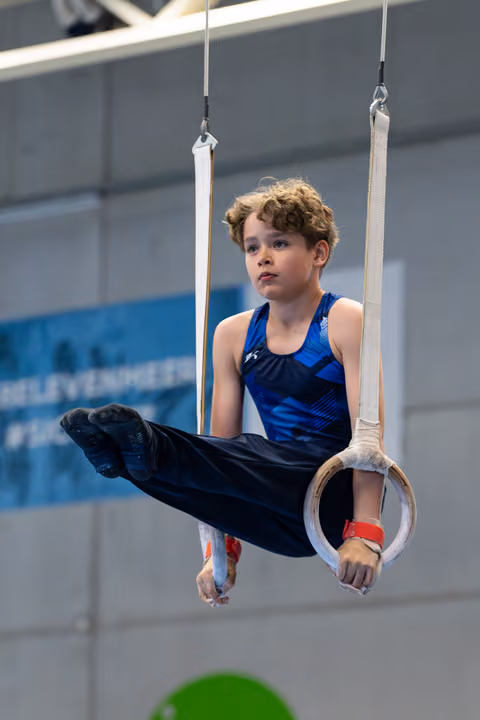 Focused young athlete performing an L-sit position on rings during training, demonstrating strength and control in a gymnasium