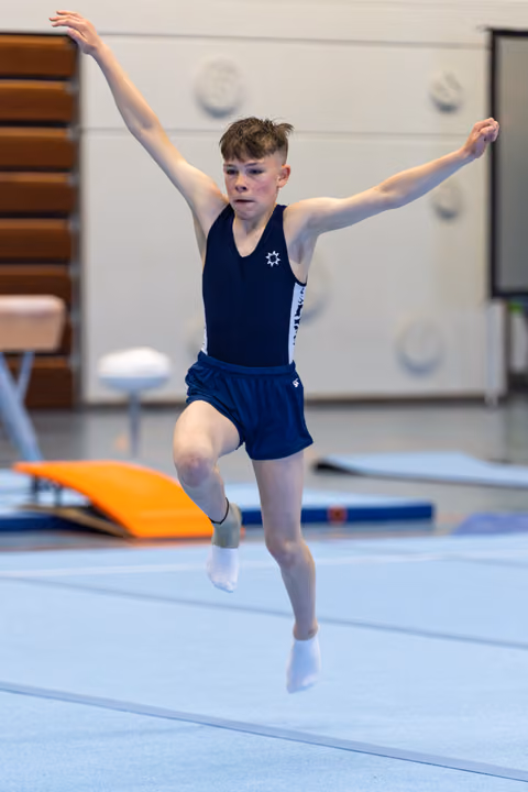 Young athlete mid-leap during floor routine with arms raised, displaying focus and grace in training facility