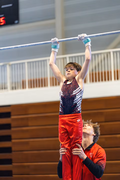 Young athlete grips the high bar while coach spots from below, arms ready to support during training routine