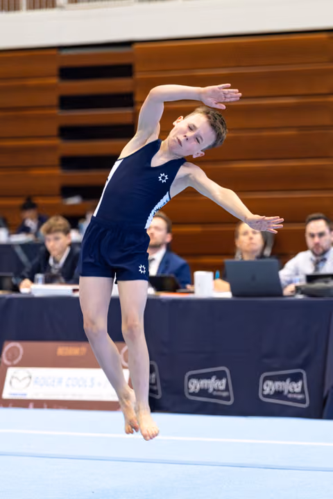 Young athlete performs expressive floor routine with graceful side bend during competition, judges seated at table in background