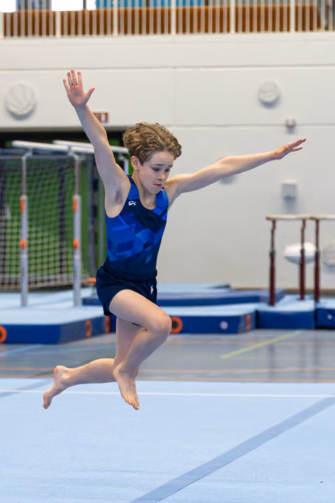 Young gymnast executing a graceful split leap during floor routine, arms extended, in indoor training facility