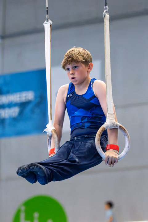 Young athlete suspended on rings during routine, displaying concentration with raised eyebrows in gymnasium setting