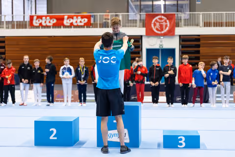 First place winner applauds from podium while other athletes stand at attention during medal ceremony in sports hall