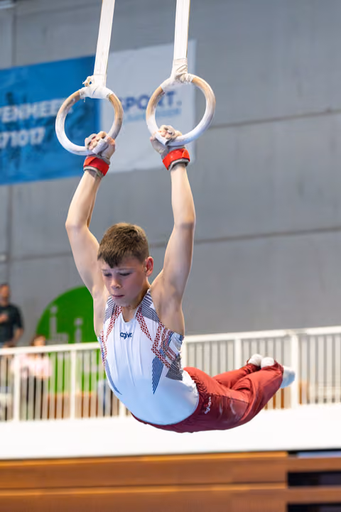 Young athlete demonstrating concentration while performing a still rings routine at an indoor sports competition