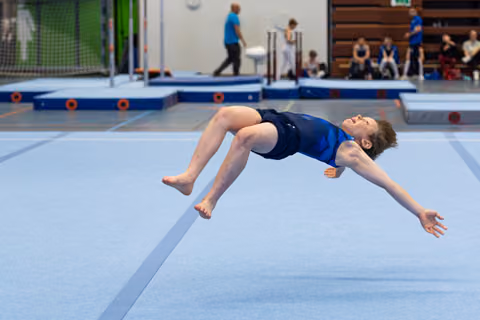 Young athlete performing a backflip mid-air on floor exercise mat during training session at indoor sports facility