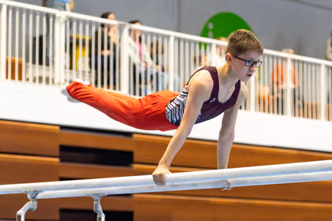 Young gymnast holds a horizontal position on parallel bars, demonstrating strength and concentration while wearing glasses