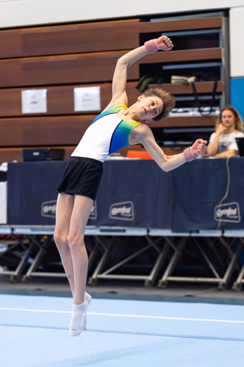 Young gymnast performs expressive floor routine with dramatic side bend, arms extended, at indoor competition venue