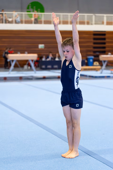 Young athlete in navy uniform stands with arms raised overhead in starting position on training floor