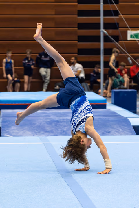 Young athlete performs backbend on floor mat during training session, demonstrating flexibility with one leg extended upward
