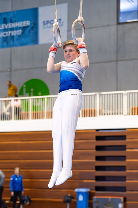 Young gymnast performing a hang position on still rings during competition, displaying focus and determination