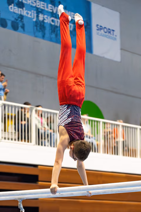 Young athlete performing a perfect handstand on parallel bars during an indoor competition with spectators in background