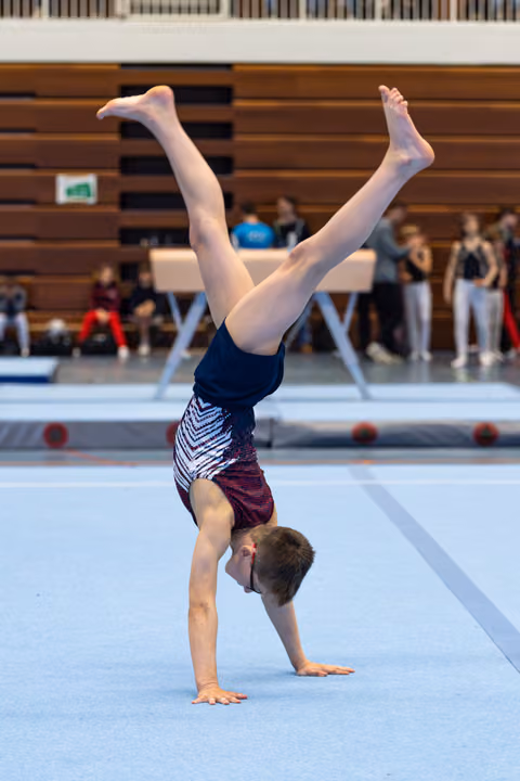 Young athlete performs a handstand with extended legs during floor routine at indoor gymnastics event