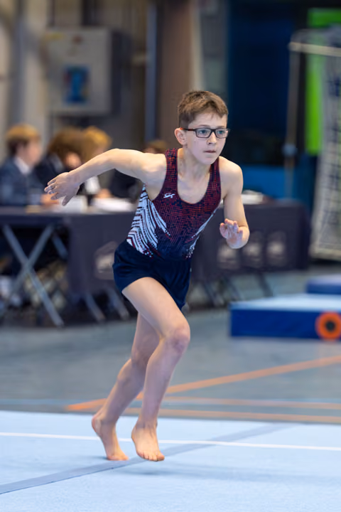 Young athlete in patterned leotard performs floor routine with focused expression and dynamic arm movement during indoor event
