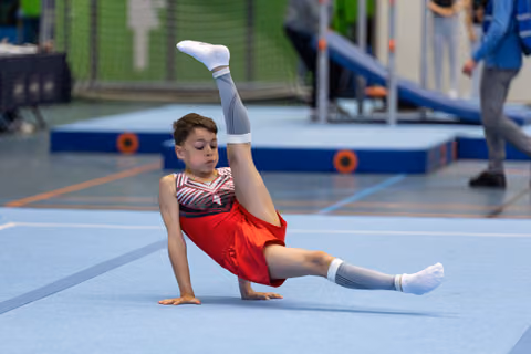 Young athlete performs floor routine with impressive split leg position, demonstrating flexibility and control on blue mat