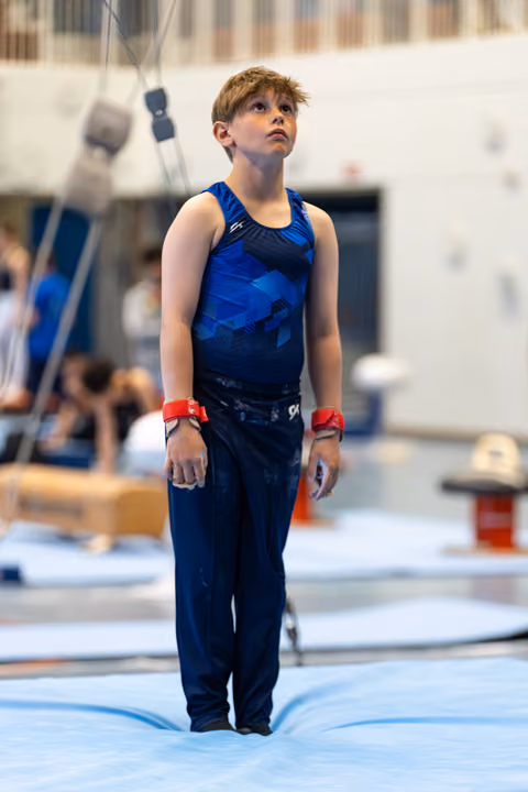 Young athlete in blue outfit with red wristbands stands attentively, gazing upward on competition floor