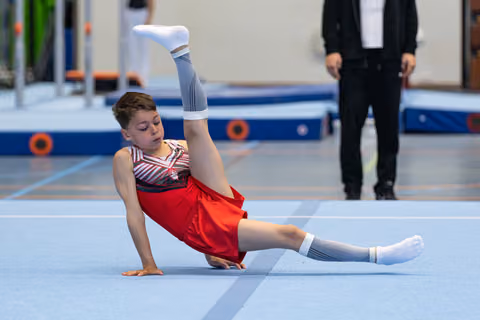 Athlete performs floor routine with leg raised vertically while seated, displaying strength and flexibility during performance