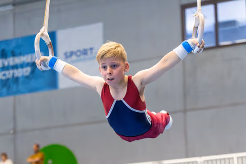 Young gymnast demonstrates strength and focus while performing on still rings at indoor training facility