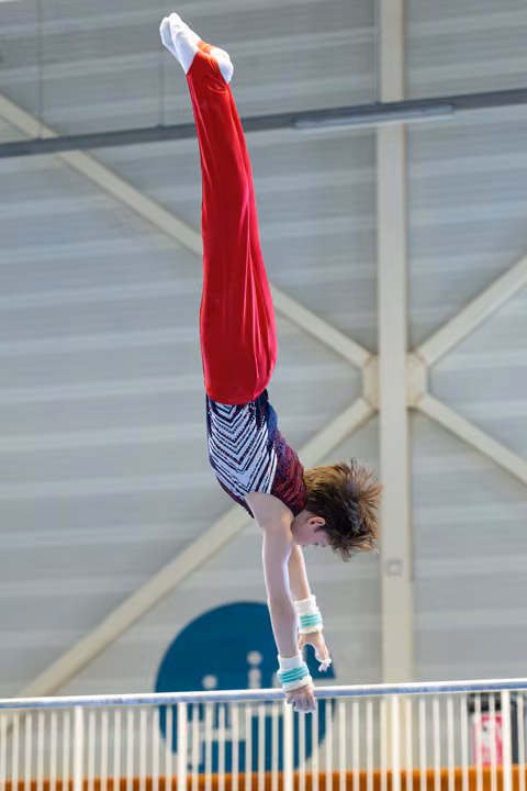 Athlete performs vertical handstand in mid-air above apparatus, body fully extended with pointed toes during routine