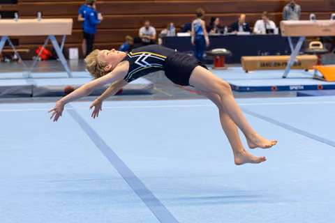 Young gymnast mid-air performing a powerful backflip during floor exercise routine in an indoor sports arena