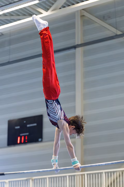 Young athlete performing handstand on parallel bars in indoor sports hall, demonstrating strength and balance