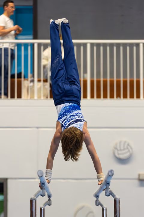 Young athlete performing a handstand on parallel bars during a routine, displaying strength and balance in competition