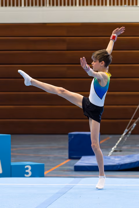 Athlete performs a front scale balance on floor, leg extended high, arms raised gracefully in colorful leotard