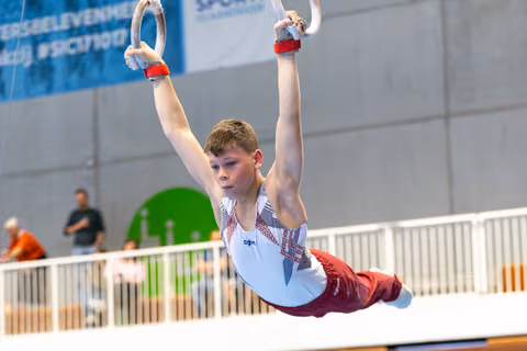 Young athlete performing a still hold position on rings during indoor competition, demonstrating strength and concentration