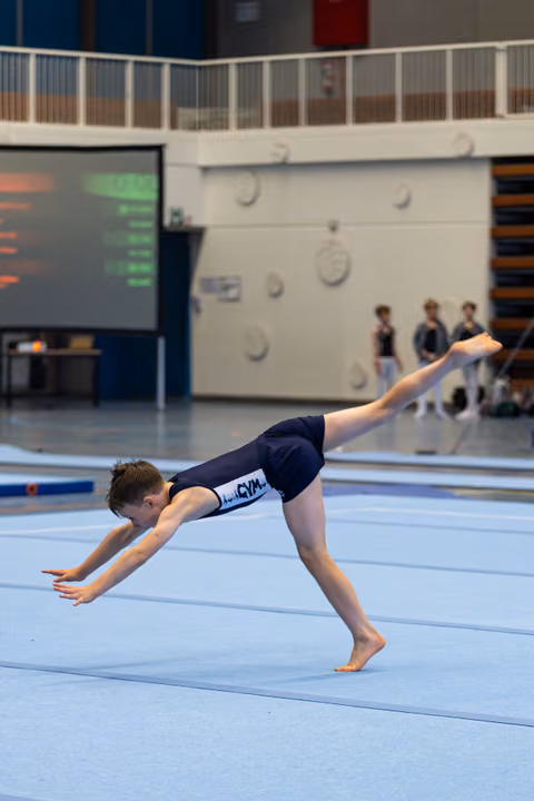 Athlete performs inverted pike position during floor routine, demonstrating strength and control on blue mat in indoor facility